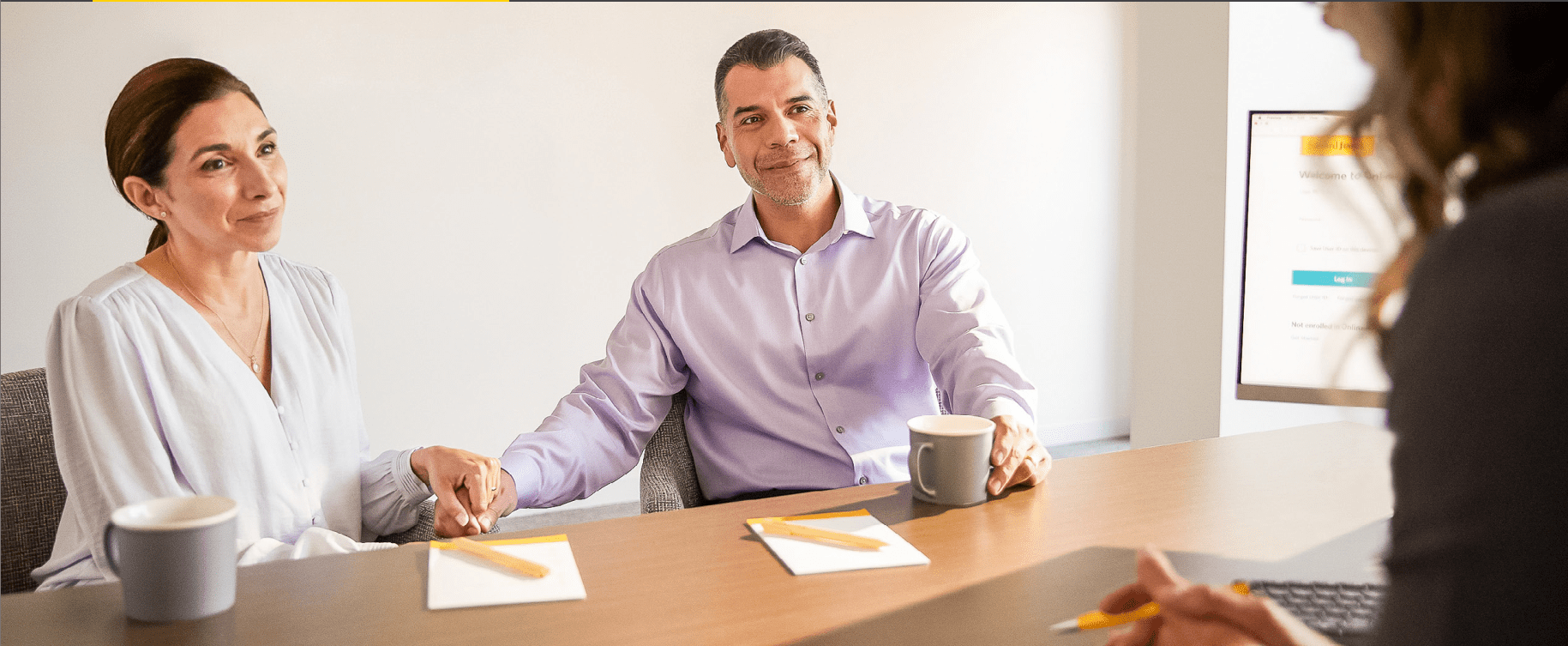 Man in purple shirt smiling at a desk with a coffee cup and papers.